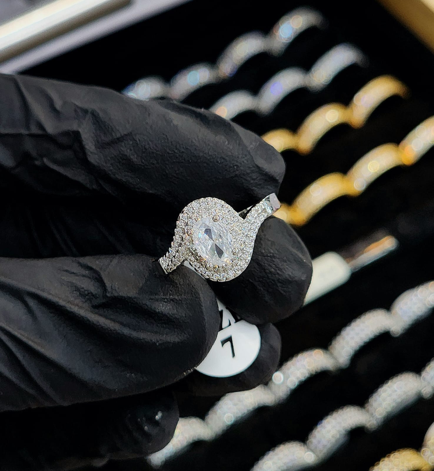 Diamond ring held by a gloved hand with a blurred jewelry display in the background